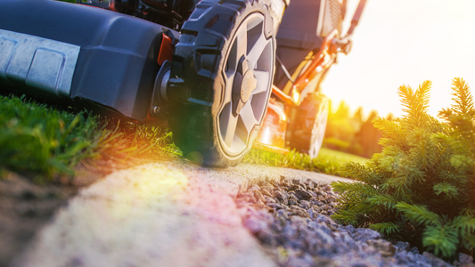 An image of a lawn mower with wheels going to the border of the grass.