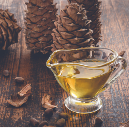 A glass pitcher of golden liquid sits on a wooden table surrounded by pinecones and seeds.