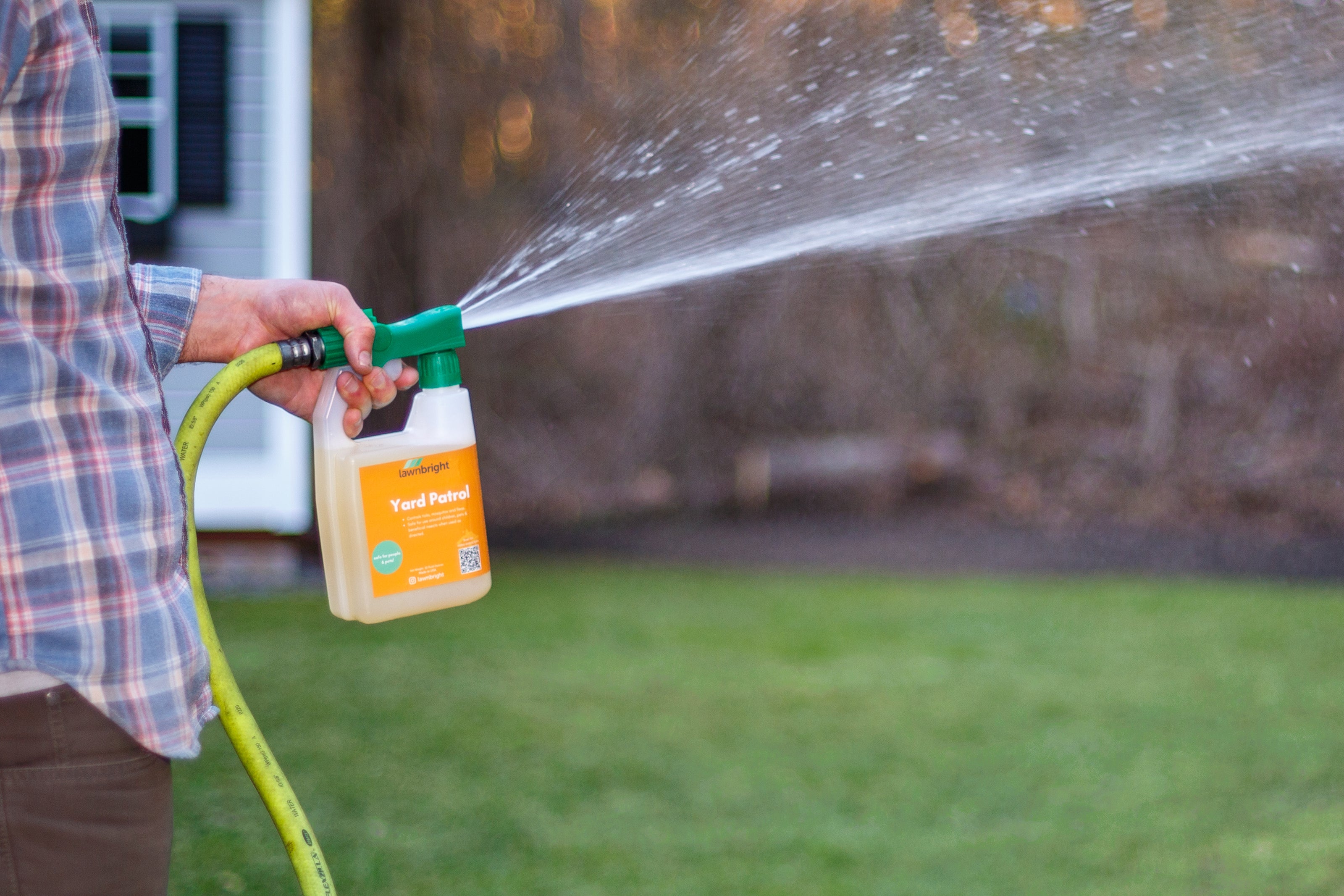 Person spraying Lawnbright Yard Patrol solution using a garden hose, green lawn in the background.