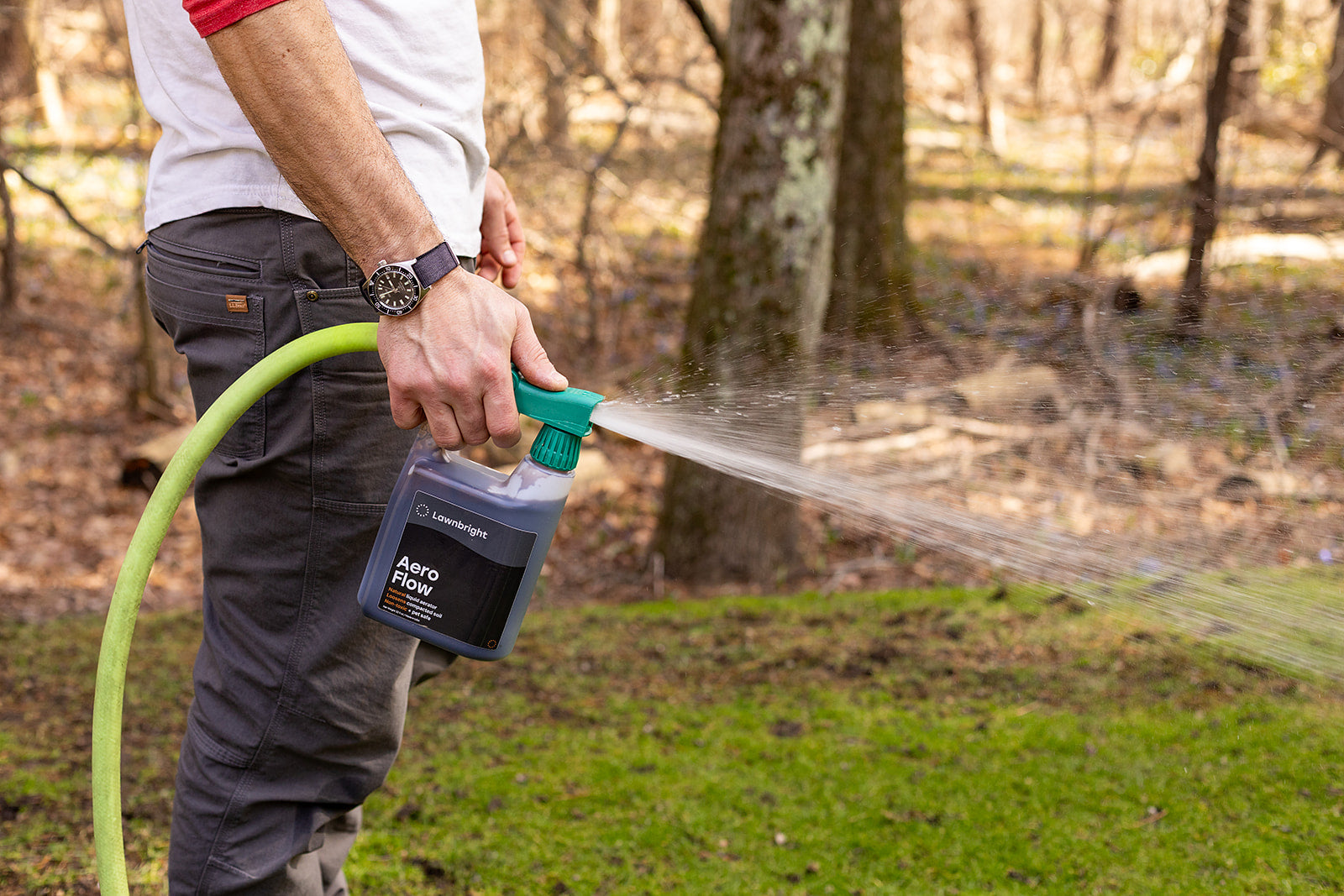 Person using a spray bottle labeled 'Aeroflow' with a garden hose outdoors.