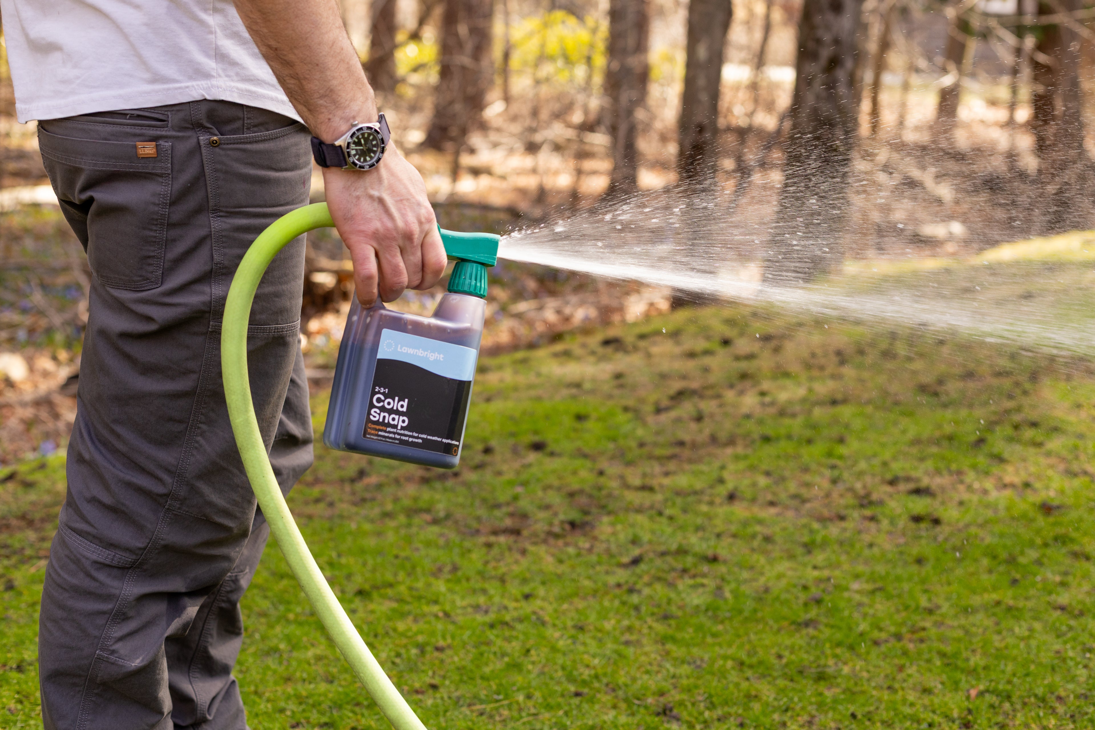Person spraying Lawnbright Cold Snap with a hose on a lawn.