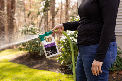 Person using a hose to spray a bottle labeled Weed Wipeout in an outdoor setting.